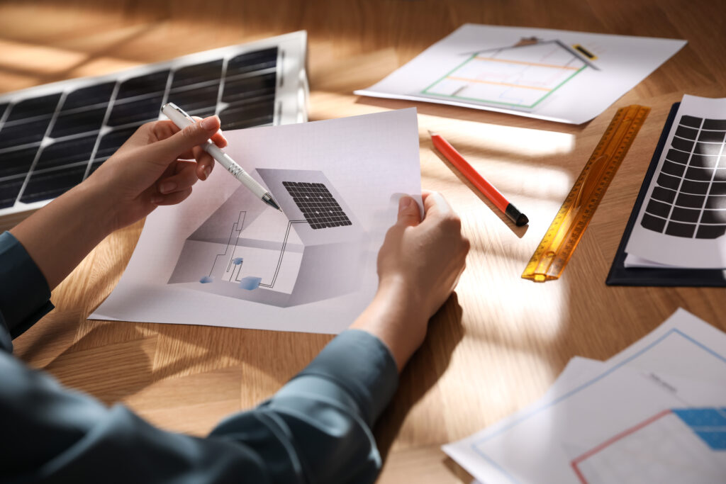 Schéma technique montrant une maison équipée de panneaux solaires photovoltaïques, avec une personne analysant le plan d’installation et les circuits électriques associés.