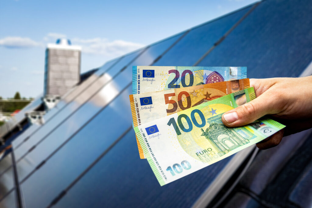 Main tenant des billets en euros devant une installation de panneaux solaires, symbolisant les économies d’énergie et les gains financiers liés au photovoltaïque.